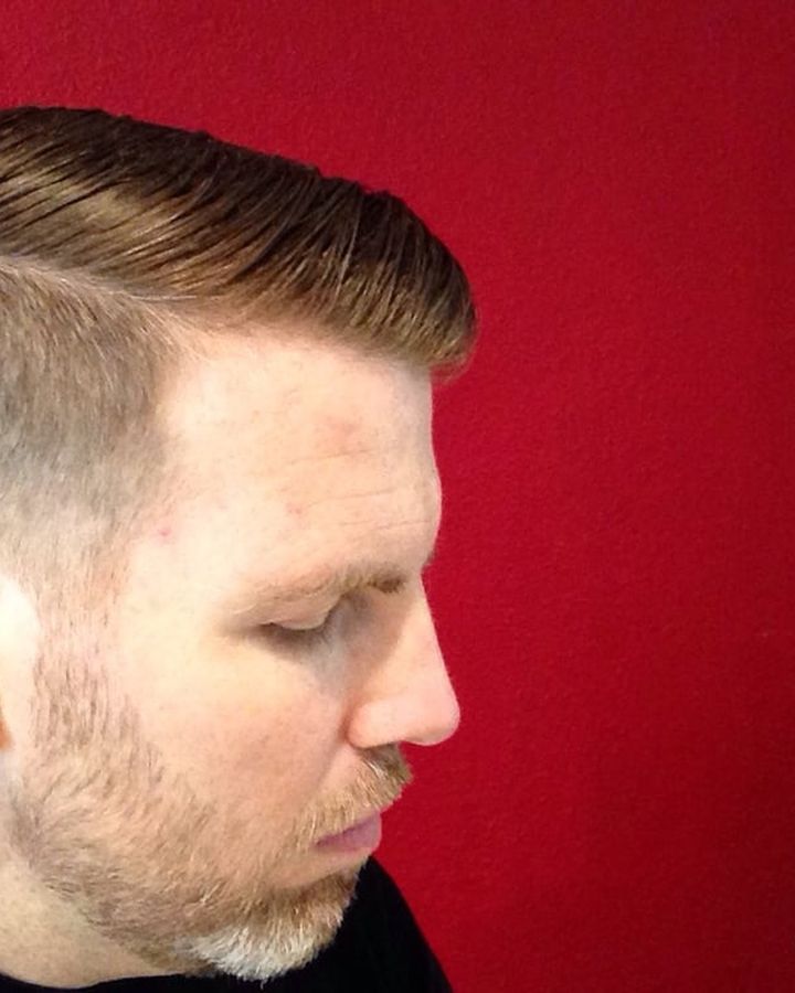 A short side part with a tapered side, photographed in profile against a red wall.