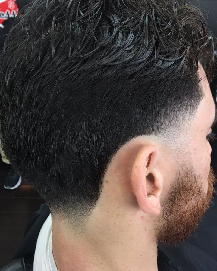 A textured top over a fade that runs down into a trimmed beard, seen from behind and to the side.