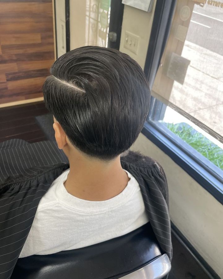 A long glossy side part combed into place, seen from behind in the chair by the window.
