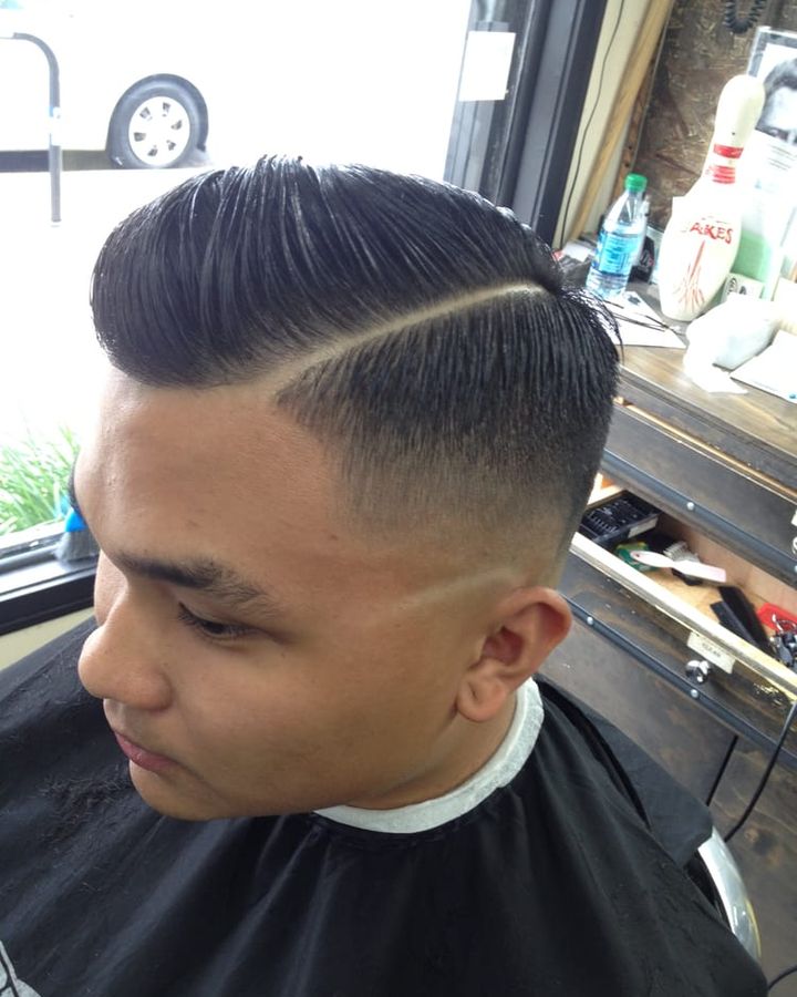 A pompadour with a hard part shaved into the side and a skin fade below it, seen from the side.