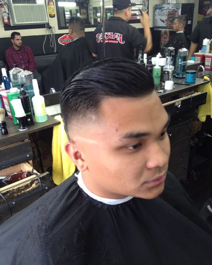 A side part combed back into a taper fade, with the shop's mirrors and stations behind.